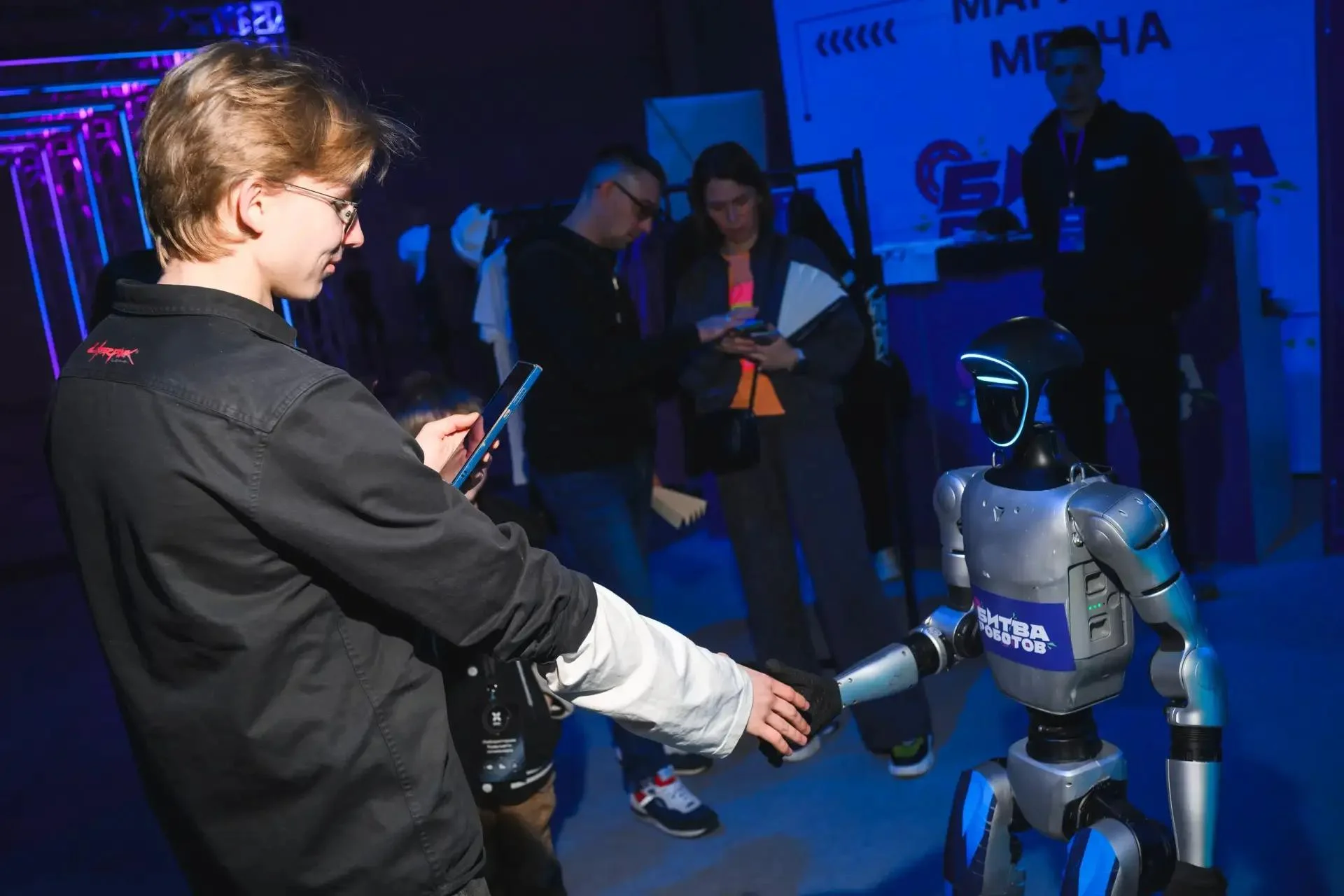 Посетитель Международного чемпионата Битва роботов пожимает руку роботу-гуманоиду